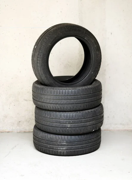 在车库里或车间堆放四个旧的旧汽车轮胎 顶部轮胎在其他轮胎上与下面有复制空间的墙相平衡 — 图库照片