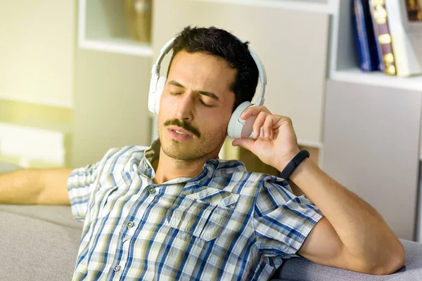 Neşeli Genç Adam Müzik Kulaklıklarıyla Müzik Dinlerken Evdeki Bir Kanepede — Stok fotoğraf