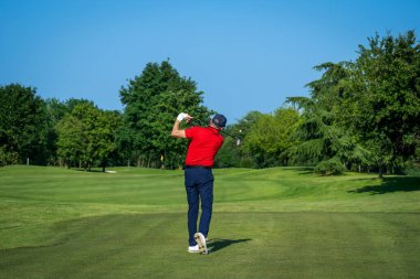 Profesyonel golfçü golf sahasında güneşli bir günde topa vuruyor.