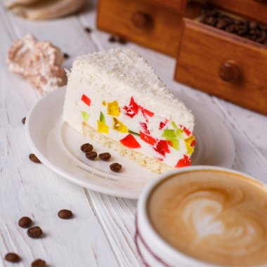 Bir tabloda bir fincan kapuçino ve kabukları ile renkli jöle ile pasta.