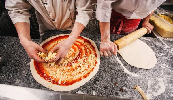 Hamur üzerinde dolgu ayrışma. Hamur masanın üzerinde. İki aşçılar iki pizza hazırlamak