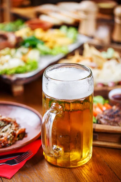Un vaso de cerveza ligera en el fondo de una mesa con aperitivos . — Foto de Stock