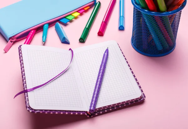 La pluma está en un cuaderno abierto, junto a un estuche de lápiz azul sobre un fondo rosa — Foto de Stock