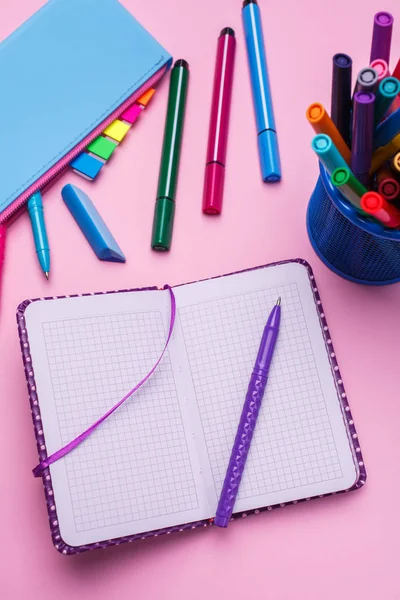 Ручка на відкритому блокноті, поруч з синім гільзою олівця на рожевому фоні — стокове фото