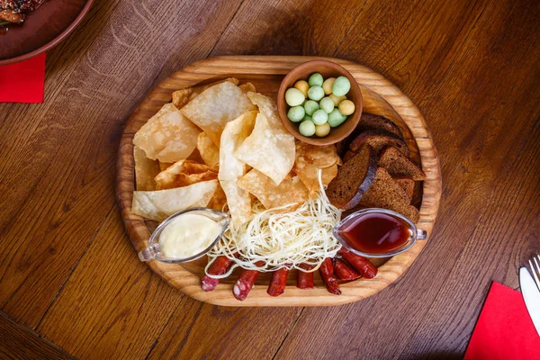 Junta con papas fritas, salchichas, pan de centeno, queso y salsa roja y blanca. Sobre una mesa de madera — Foto de Stock