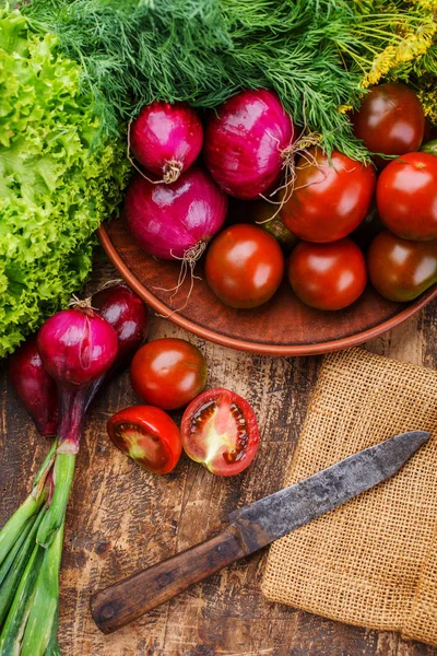 Tomatoes, onions and herbs lie next to an old wooden knife — Stock Photo, Image