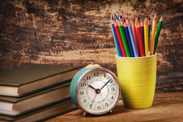 Colored pencils in a glass next to books and watche — Stock Photo, Image
