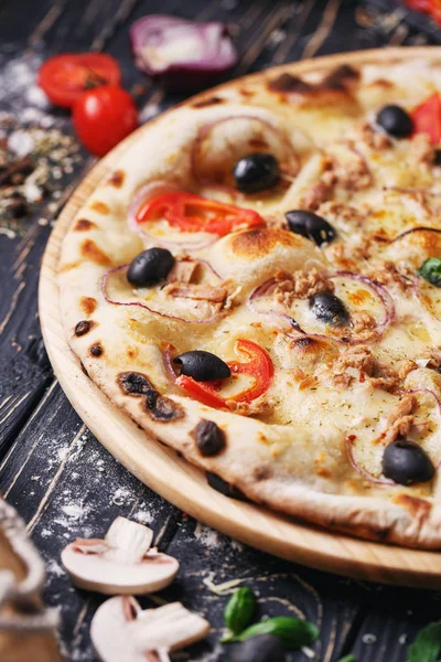 Pizza with fish, olives, onions and tomatoes near vegetables