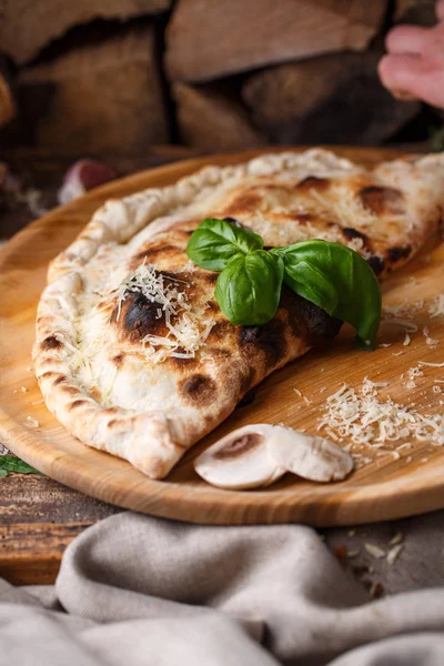 Pizza Calzone doblado por la mitad está decorado con albahaca en el fondo de la leña —  Fotos de Stock