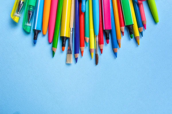 Plumas de colores, lápices, marcadores y otros objetos se encuentran sobre un fondo azul claro . —  Fotos de Stock