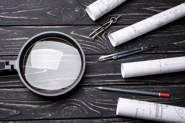 Magnifying glass with drawing tools and rolls drawings on a blac — Stock Image Magnifying glass with drawing tools and rolls drawings on a blac Royalty Free Stock Photos