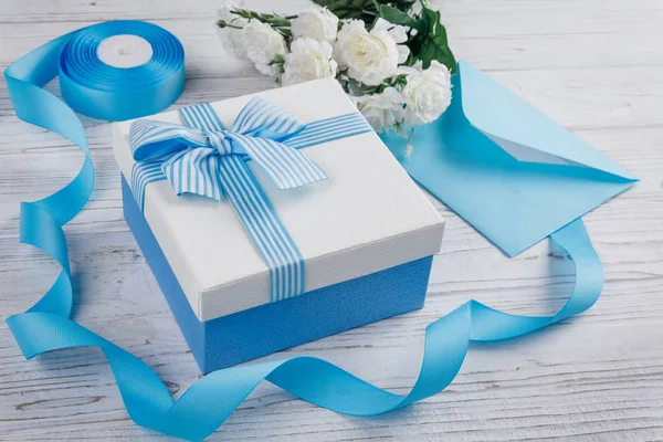 Gift box with bow. Blue satin ribbons and letter. Flowers in the background. — Stock Photo, Image