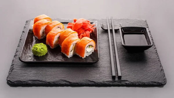 Japanese sushi on a dark stone background. Sushi set with ginger, wasabi and soy sauce. Serve with chopsticks. Black background. Asian or Japanese food frame.