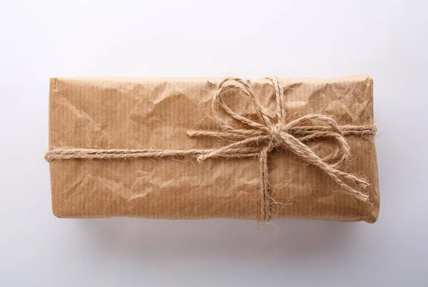 Cadeau enveloppé dans du papier kraft et un ruban de toile de jute sur fond blanc. Vue du dessus. — Photo