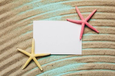 Turkuaz arka planda deniz yıldızı yazılı beyaz boş kart. Dalgalı desenli kum. Üst görünüm.