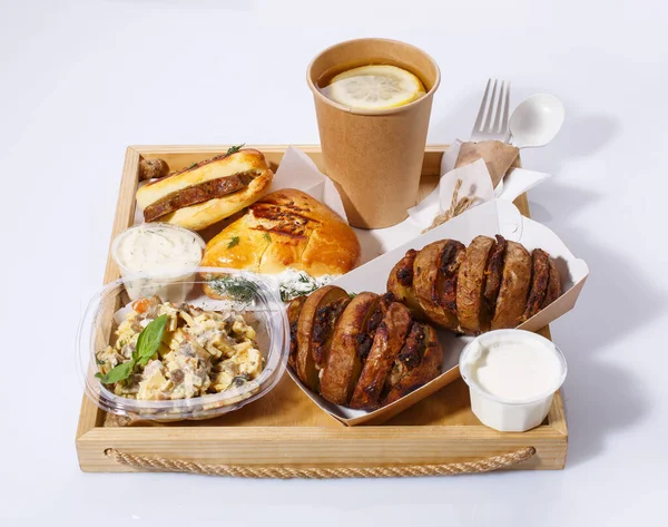 Almoço delicioso com utensílios descartáveis em bandeja de madeira. Chá de limão, salada, batatas assadas com carne, molho e pães. — Fotografia de Stock