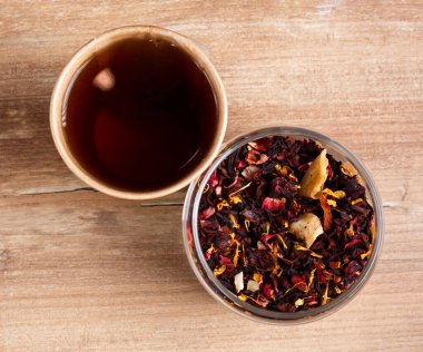 Bir bardak Karkade çayı ve tek kullanımlık kağıt bardakta demlenmiş çay, ahşap kırsal arka planda. Üst görünüm.