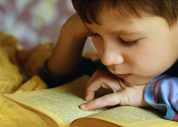 Boy is reading a book lying on a bed — Stock Photo, Image