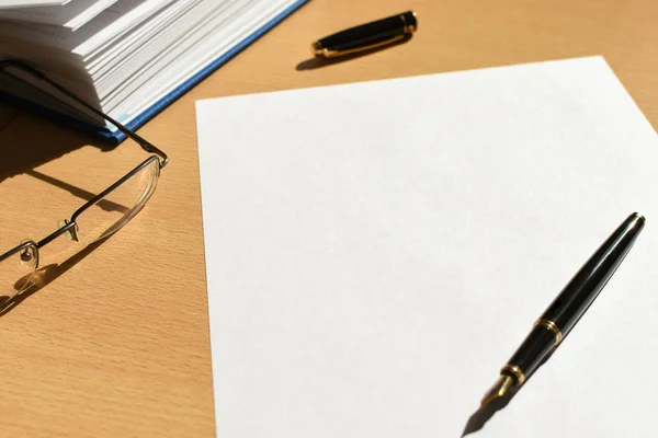 White sheet of paper on a wooden desktop in the office, pen, accessories, glasses, copy space — Stock Photo, Image