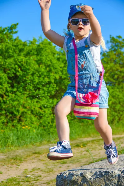 Küçük kız oynuyor bir çiçek ile onun elinde bir yükseklikten atlama gülümseyen