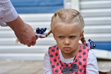 Sad little girl sits and waits while mom braids her hair from her hair clipart