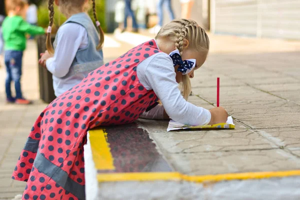 Petite fille apprendre à dessiner avec un crayon sur un morceau de papier de magazine enfants dans la cour de l'école — Photo
