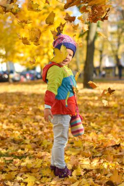 Parlak elbiseleri ile oynarken mutlu küçük kız bir şehir parkında sonbaharda yaprakları.