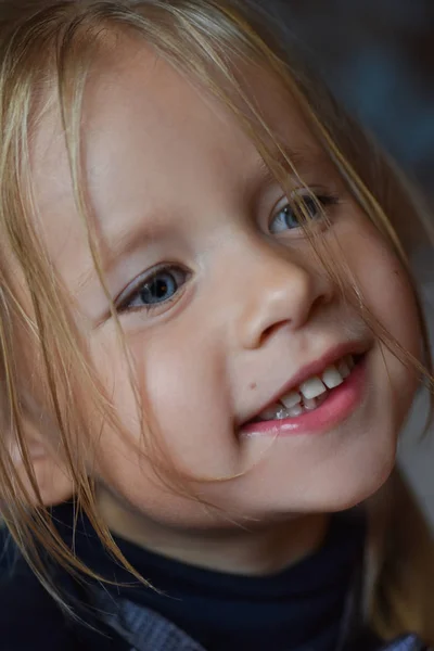 Portræt af en munter romantisk lille pige med store blå øjne og et åbent smil fra Østeuropa, close-up, mørk baggrund - Stock-foto