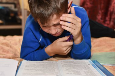 Teenager cries while solving a difficult school homework in a room on a bed clipart
