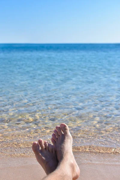 Feet in the sand on the beach against a blue sea — Zdjęcie stockowe