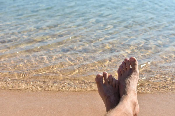 Feet in the sand on the beach against a blue sea — Stockfoto