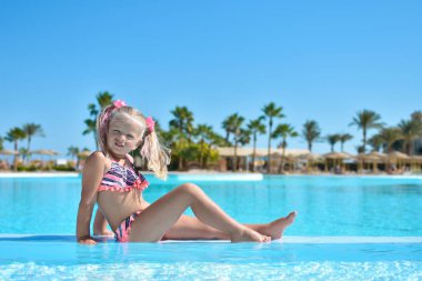 Palmiye ağaçları ile bir otel bir yüzme havuzunda masmavi suda bir kız bir mayo içinde oturur