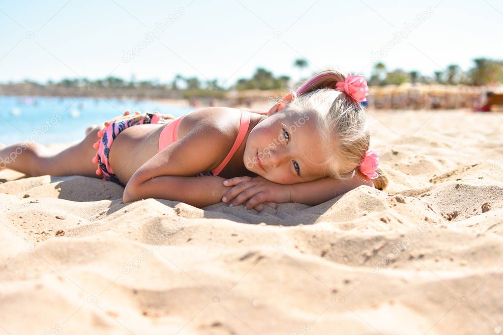 The girl lies on the beach sand near the sea and sunbathes