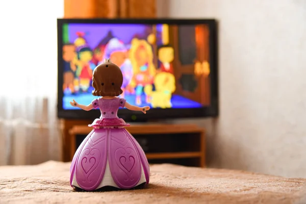 Oyuncak bebek pembe elbiseli bir karikatür TV izliyor