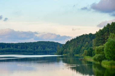 Gün batımında bir orman gölünün kıyısında yatıyor..