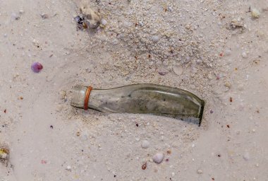 Boş bir cam şişe sudaki kumun üzerinde yatıyor.