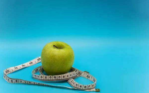 a green ripe juicy apple and a white measuring tape around it on a clean light blue background with space for copy wright text