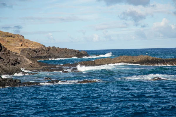 Tenerife İspanya 'sında deniz köpüğü ve Atlantik Okyanusu dalgaları kayalara çarpıyor. Ufkun üzerinde desenli bulutlarla gökyüzü