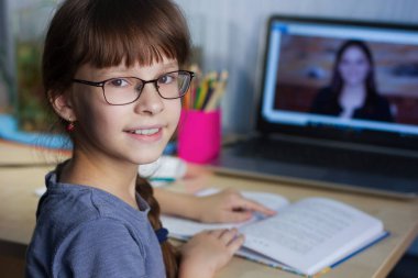 Uzaktan öğrenme çevrimiçi eğitim. Mutlu bir kız evde okuyor ve okul ödevlerini internetten yapıyor.