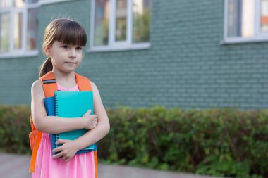 Sırt çantalı küçük kız elinde defterler tutuyor.