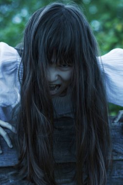 Uzun siyah saçlı korkunç hayalet kız ağzını açar ve bağırır.