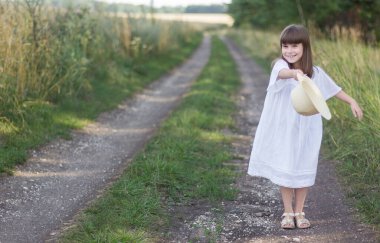 Küçük kız, çavdar tarlasının yanındaki yolda şapkasıyla oynuyor..