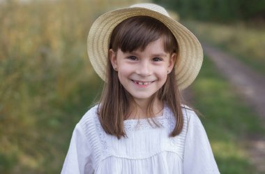 Yoldaki mutlu küçük kız. Beyaz elbiseli tatlı, gülümseyen kız tarlanın yanında duruyor.