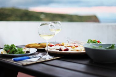 Beyaz şarap kadehleri ve dağların arka planında, Portekiz 'deki Azores adalarında bir masada bir peynir tabağı.