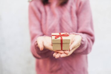 Kadının elinde kırmızı kurdele, arka planında pembe süveter olan el işi kutusu.