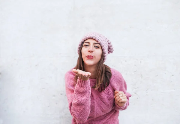Pembe örgü şapkalı ve kazaklı güzel esmer kadın hava öpücüğü yolluyor. Düz gri arkaplan