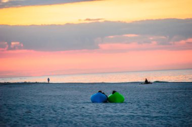minder üzerinde gün batımı sırasında deniz kenarında oturan iki kişi ile yatay çerçeve