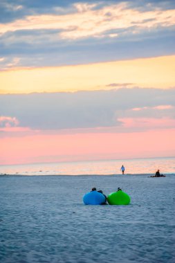 minder üzerinde gün batımı sırasında deniz kenarında oturan iki kişi ile yatay çerçeve