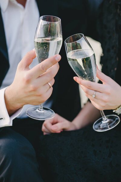 Hands of elegant man and woman cheering with glasses of white wine