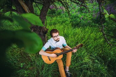 Romantik kavramı. Genç adam acı bakla bir arka plan üzerine açık ağacının altında gitar çalmak.